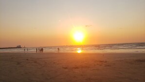 Une plage au coucher du soleil, avec le soleil bas à l’horizon, des gens se promenant le long du rivage et des vagues douces sur l’océan.