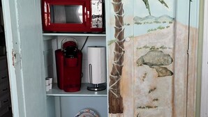 Une pièce avec un meuble blanc orné d’une fresque aux motifs tropicaux, un micro-ondes rouge et une machine à café.