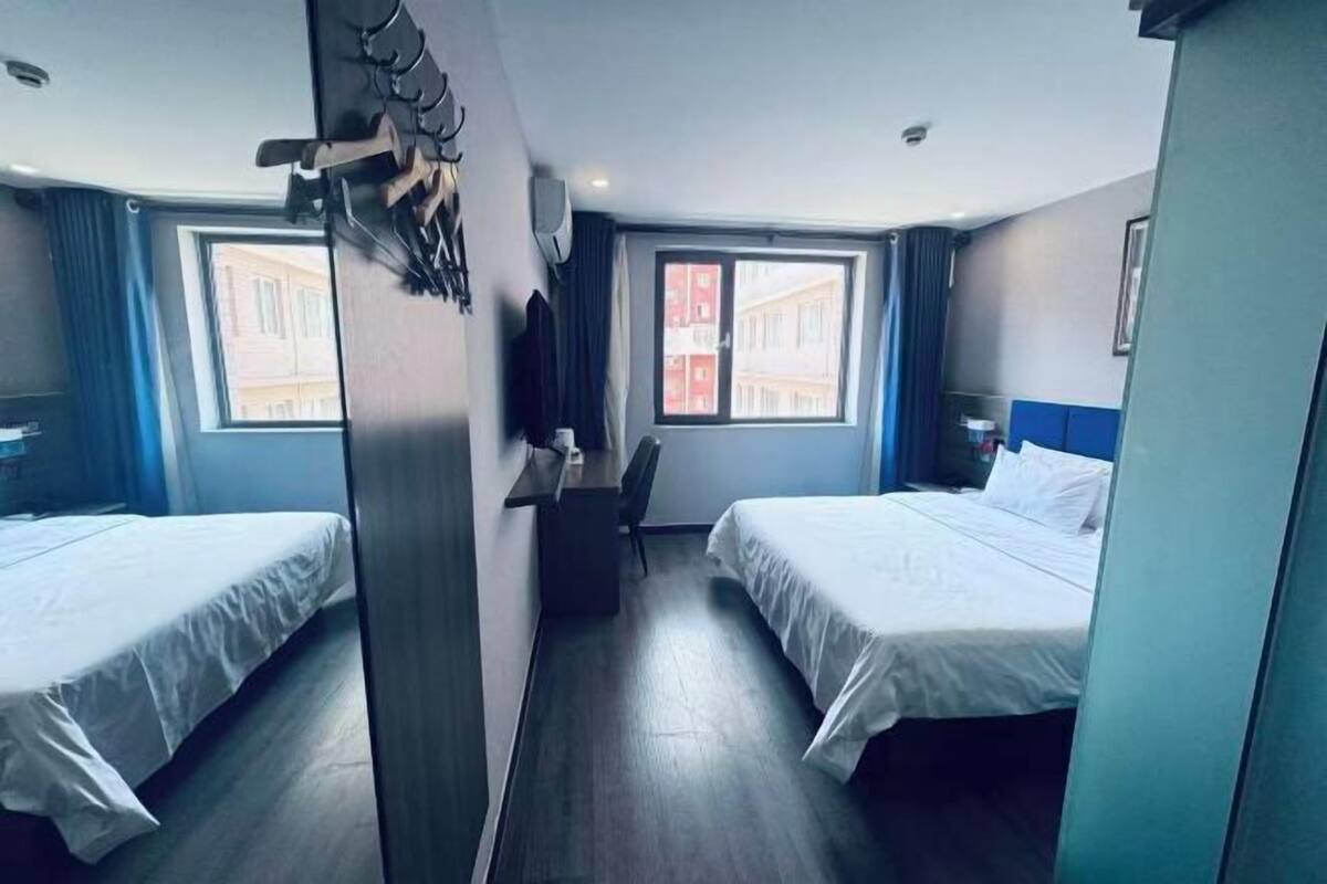 Une chambre d’hôtel avec deux lits, un bureau, une chaise et une fenêtre donnant sur des immeubles.
