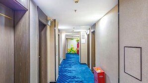 Un couloir d’hôtel avec un tapis bleu, des portes en bois et un objet rouge sur la droite.
