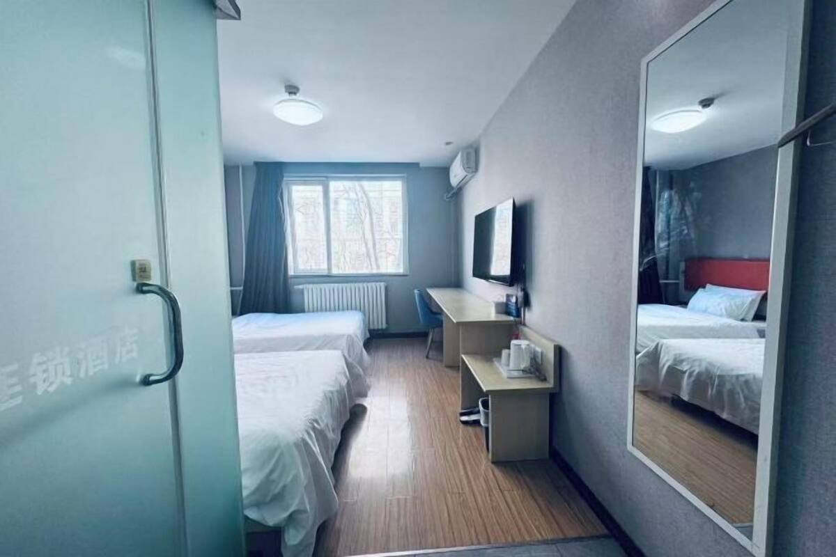 Une chambre d’hôtel avec deux lits, un bureau, un miroir, une télévision et une fenêtre.