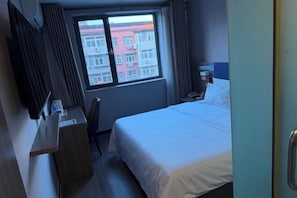 A hotel room with a bed, a desk, a chair, a nightstand, a TV, and a window with a view of buildings. - 7 Days Premium Hotel (Beijing Zhongguancun Renmin University Suzhoujie Subway Station) (Beijing)