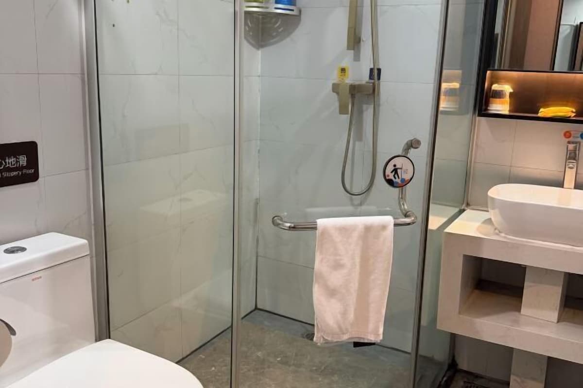 A modern bathroom with a glass shower enclosure, a toilet, and a sink with a towel rack.