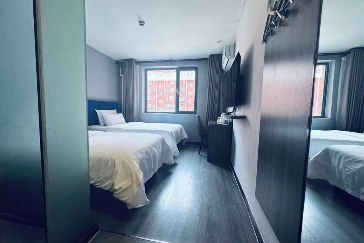 Une chambre d’hôtel avec deux lits, un bureau, une fenêtre avec des rideaux et une armoire.