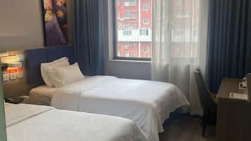 Habitación de hotel con dos camas, un escritorio, una silla, un cuadro en la pared y una ventana con cortinas.