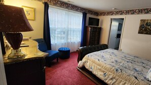 A hotel room with a bed, a desk with a lamp, a chair, a TV, and a window with curtains.