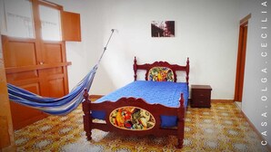 A bedroom with a wooden bed, a hammock, a small bedside table, and patterned floor tiles. - Casa Olga Cecilia (Honda)