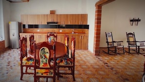 A dining area with a round wooden table and chairs, a kitchen in the background, and a patterned floor. - Casa Olga Cecilia (Honda)
