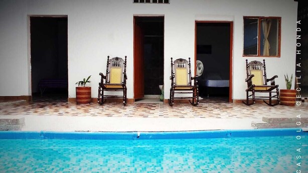 A poolside area with two wooden chairs and potted plants, a tiled floor, and a blue pool. - Casa Olga Cecilia (Honda)