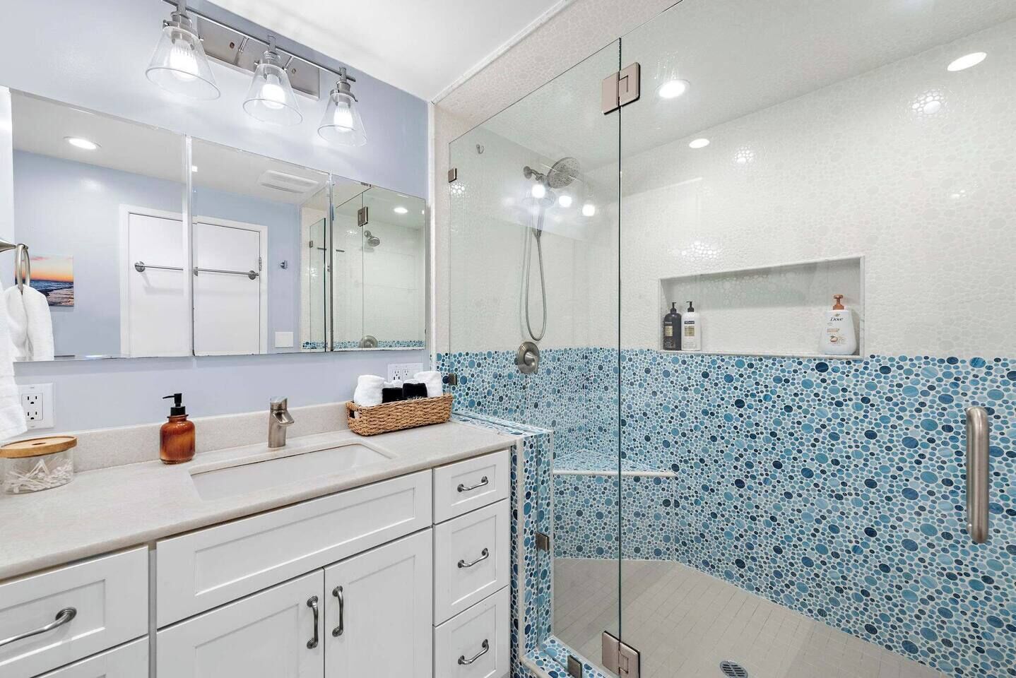 A modern bathroom with a glass-enclosed shower, a large mirror, and a tiled backsplash.