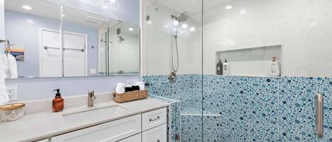A modern bathroom with a glass-enclosed shower, a large mirror, and a tiled backsplash.
