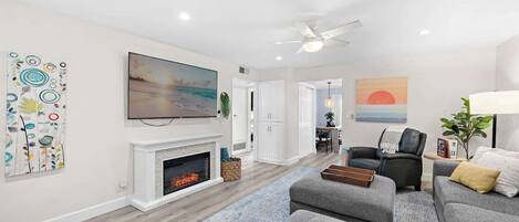 A modern living room with a fireplace, a television, and a ceiling fan.