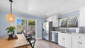 Una cocina moderna con armarios blancos, un refrigerador de acero inoxidable y una mesa de comedor de madera con sillas.