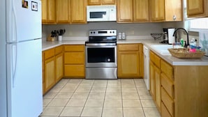 A kitchen with wooden cabinets, a stainless steel refrigerator, a microwave, and an oven. - Sunshine Shack - 2 bedroom, In-Town, Dog Friendly, Near the Beach! (Port Aransas)
