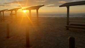 A beach with wooden structures and the sun setting in the background. - Sunshine Shack - 2 bedroom, In-Town, Dog Friendly, Near the Beach! (Port Aransas)