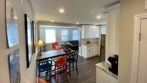 Une cuisine moderne avec des meubles blancs, un coin repas avec une table et des chaises, et un salon avec un canapé et une table basse.