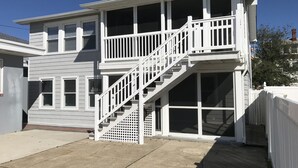 Une maison à deux étages, avec une façade blanche, un porche à l’avant et un escalier menant à l’étage supérieur.