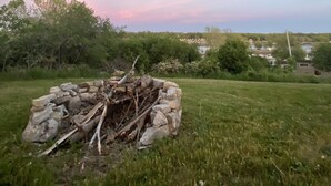 Un foc a terra de pedra envoltat d'herba i arbres, amb vista a una població llunyana i un cel serè.