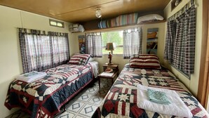 Una cabana amb dos llits, cadascun amb un edredó acolxat, una taula petita amb una làmpada i una finestra amb cortines.