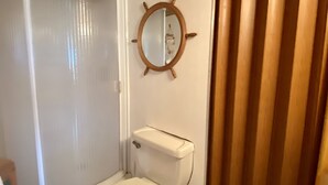 Un bany compacte amb vàter, un petit lavabo i un mirall amb disseny de timó de vaixell.