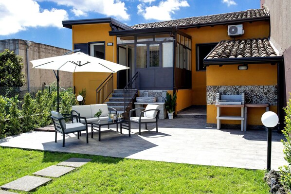 Una casa moderna con un patio, mobiliario exterior y una escalera que lleva a un nivel superior.