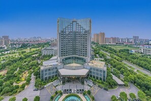 A high-rise hotel with a modern glass facade, surrounded by greenery and a clear sky. - Jinyue International Hotel Jinjiang (Jingjiang)