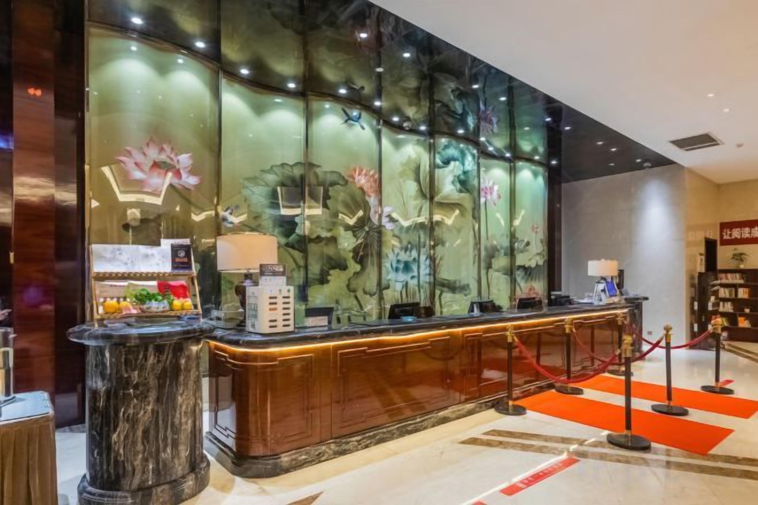 A reception desk with a glass partition, a red rope barrier, and a decorative wall with floral patterns.