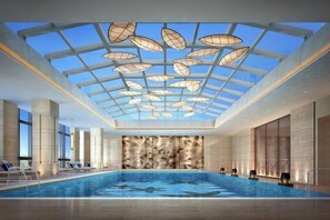 Ein moderner, überdachter Innenpool mit Glasdach und einer gemusterten Wand im Hintergrund.