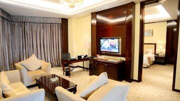 A hotel room with a TV, a desk with a computer, a sofa, and a bed.