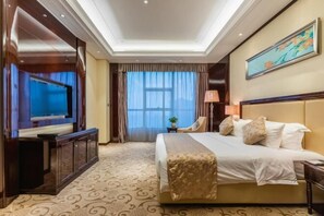 Una habitación de hotel con una cama grande, televisión, escritorio y ventana con cortinas.