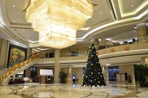 A spacious lobby with a large Christmas tree, a grand chandelier, and a staircase.