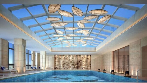 Une piscine intérieure moderne dotée d’un toit en verre et de luminaires en forme de feuilles.