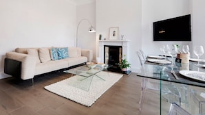 A modern living room with a sofa, glass coffee table, and a fireplace. - Modern and Bright Highgate Gem (London)