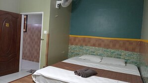 A bedroom with a bed, a wooden door, a wall-mounted fan, and a green and yellow painted wall. - Aeon Tebrau Apartment Johor Bahru (Johor Bahru)