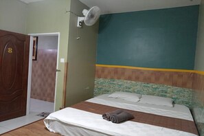A bedroom with a bed, a wooden door, a wall-mounted fan, and a green and yellow painted wall. - Aeon Tebrau Apartment Johor Bahru (Johor Bahru)