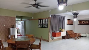 Un comedor con una mesa redonda y sillas, un ventilador de techo, y una cocina visible a través de un vano abierto.