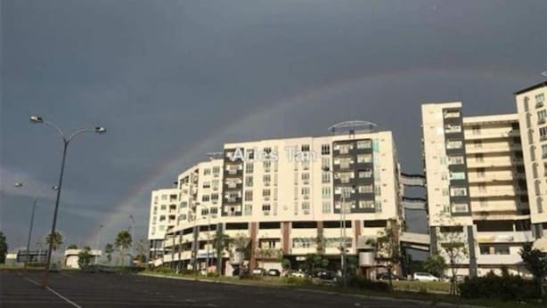 Un edificio de varios pisos con techo plano y balcones, rodeado por un estacionamiento y farolas.