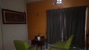 A room with two green chairs, a small table with a potted plant, a curtain, and a framed picture on the wall. - Aeon Tebrau Apartment Johor Bahru (Johor Bahru)