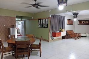Uma área de refeições com mesa redonda e cadeiras, um ventilador de teto e um candeeiro fixado na parede.
