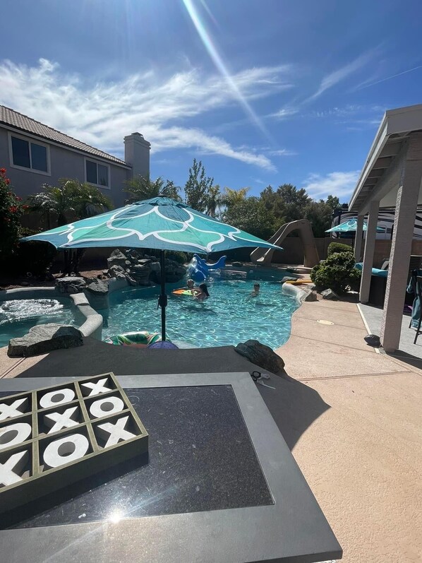 A pool area with a slide, umbrellas, and a game table. - Renovated WATERSLIDE private Heated pool with Spa Golf Course on-call service  (Mesa)