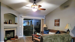 A living room with a fireplace, a ceiling fan, a couch, and a table with decorative items. - Renovated WATERSLIDE private Heated pool with Spa Golf Course on-call service  (Mesa)
