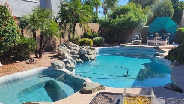 A swimming pool with a rock-lined edge, surrounded by palm trees and a house. - Renovated WATERSLIDE private Heated pool with Spa Golf Course on-call service  (Mesa)