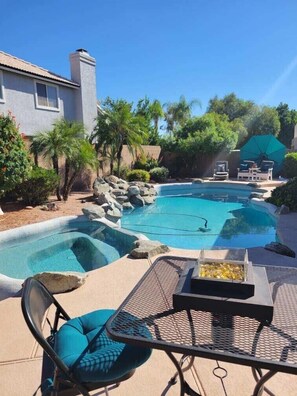 A swimming pool with a rock-lined edge, surrounded by palm trees and a house. - Renovated WATERSLIDE private Heated pool with Spa Golf Course on-call service  (Mesa)