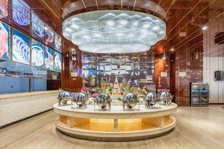 A lobby with a central round counter, a large chandelier, and artwork on the walls.. Xixia International Hotel