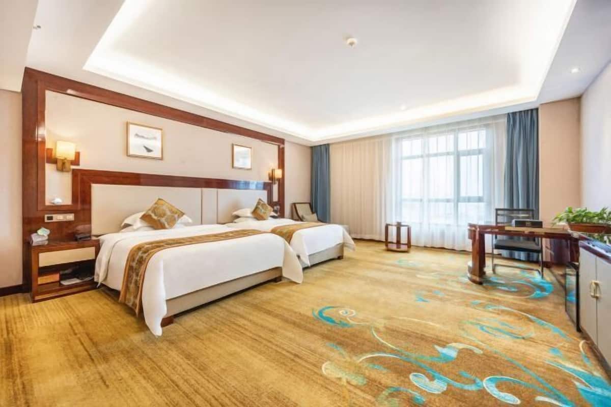 A hotel room with two beds, a desk, and a large window with curtains.