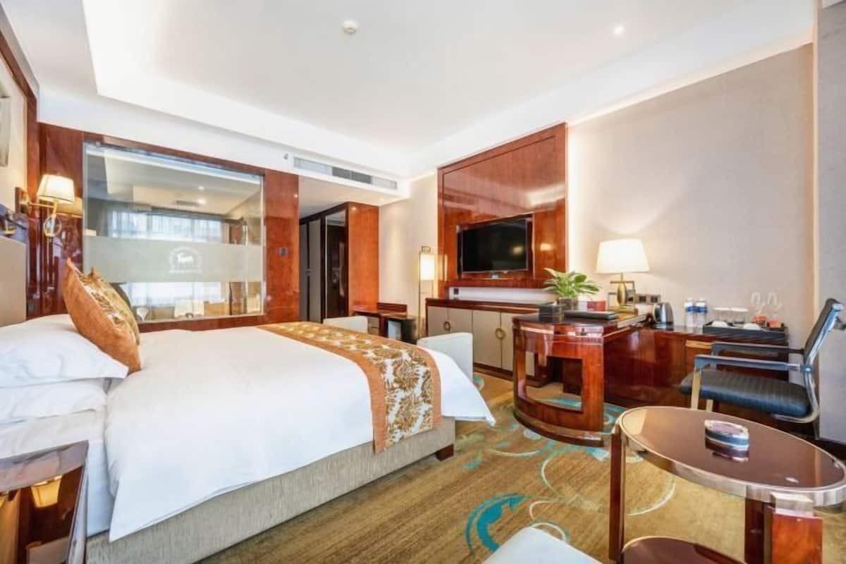 A hotel room with a large bed, a desk with a TV, and a seating area.