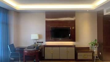 Habitación de hotel con una televisión de pantalla plana grande montada en la pared, un escritorio con una silla, una mesita auxiliar pequeña y una planta en maceta.