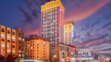 A cityscape with high-rise buildings, one with illuminated signage, and a busy street with moving vehicles.