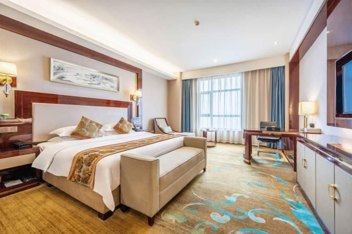 A hotel room with a large bed, a desk, a chair, a TV, and a window with curtains.