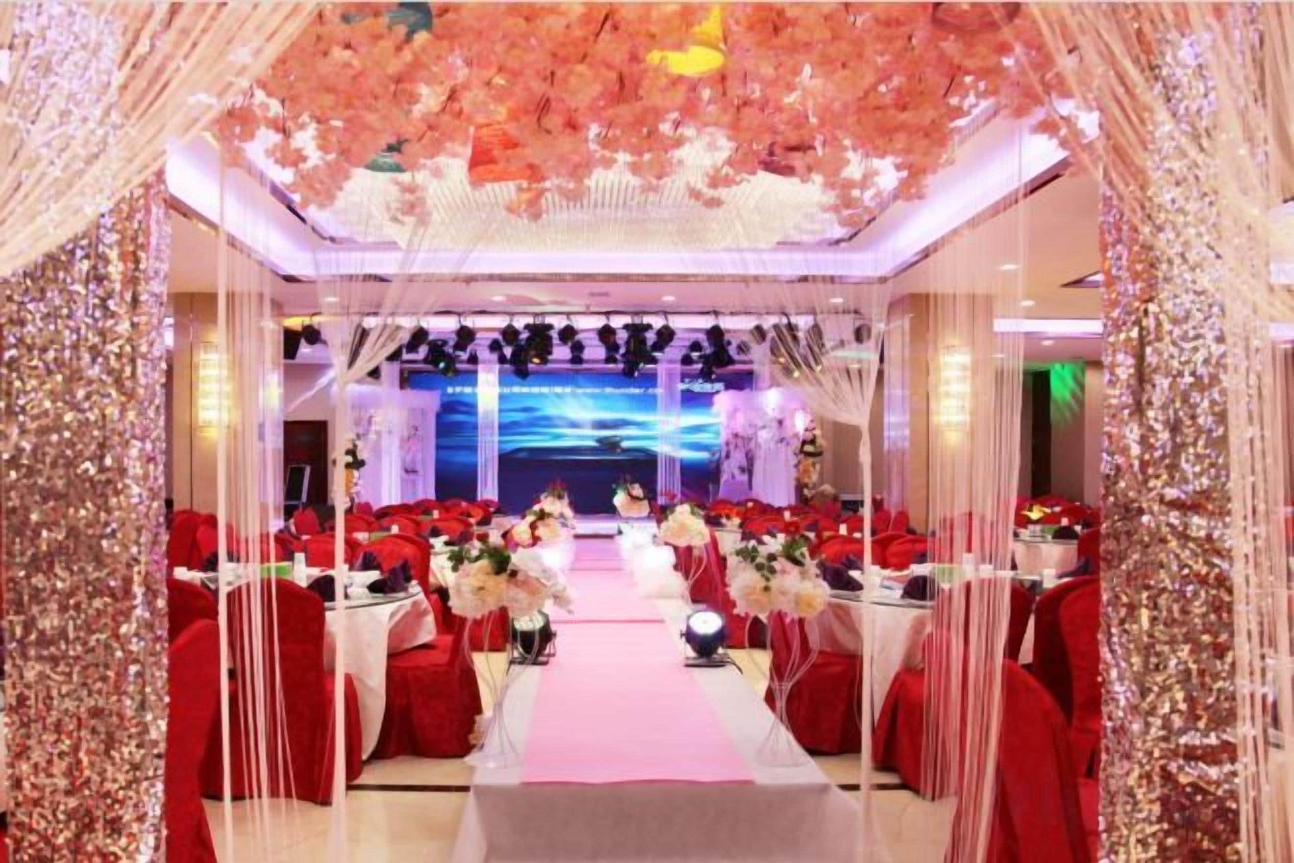 A banquet hall with a long table, red chairs, and floral decorations.